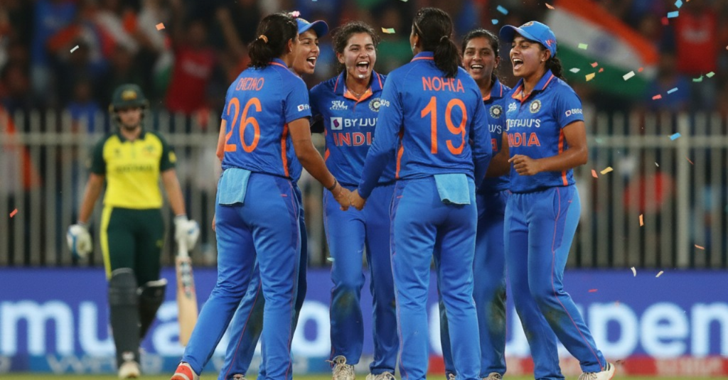 Indian women cricketers celebrating after a wicket against Australia, with vibrant team jerseys, Indian flag in the stands, confetti in the air, realistic lighting, captured in dynamic motion with focus on emotion and unity — realistic sports photography.